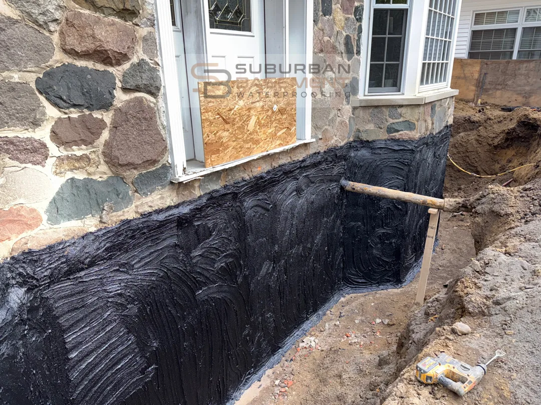 Bituminous tar coating applied to exterior stone foundation wall during waterproofing excavation in Franklin Oakland County Michigan — Suburban Basement Waterproofing
