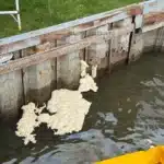 Polyurethane foam surfacing through holes in a canal seawall in Harrison Township MI, contained by a turbidity barrier
