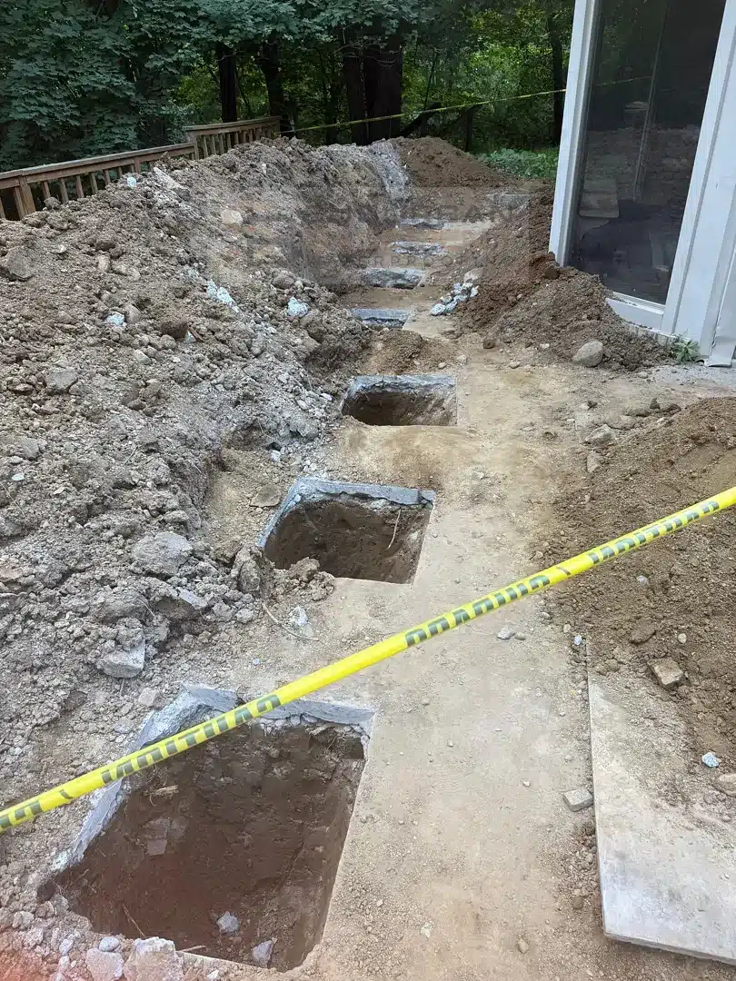 Excavated pits for buried earth anchors in the patio area behind a retaining wall in Farmington Hills MI