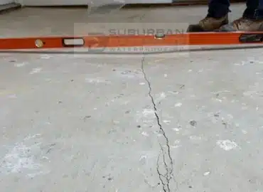 Level across a cracked, settled condo living room concrete slab in Troy MI before void filling and concrete leveling