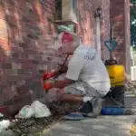 Technician injecting through a lance while foam builds up at the base of a brick garage wall during deep injection in Warren MI