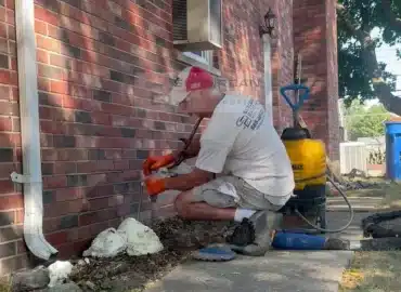 Technician injecting through a lance while foam builds up at the base of a brick garage wall during deep injection in Warren MI